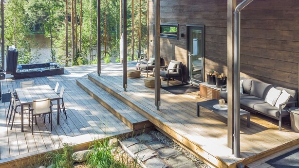 Una terraza de madera con mobiliario exterior, un jacuzzi y una pantalla de televisión.