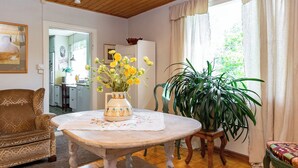 A cozy living room with a wooden ceiling, a dining table with a vase of flowers, a sofa, and a large potted plant. - Vacation home Muhola by Interhome (Enonkoski)
