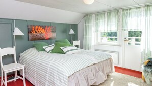 A bedroom with a bed, a chair, a radiator, a window with curtains, and a painting on the wall. - Vacation home Muhola by Interhome (Enonkoski)