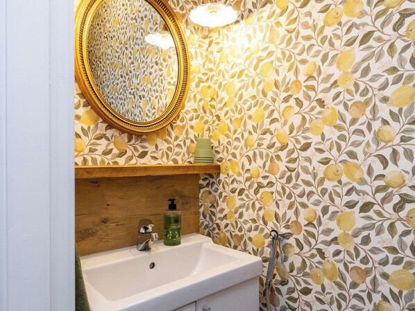 A bathroom with a white sink, a mirror with a gold frame, and a wall with a floral pattern.