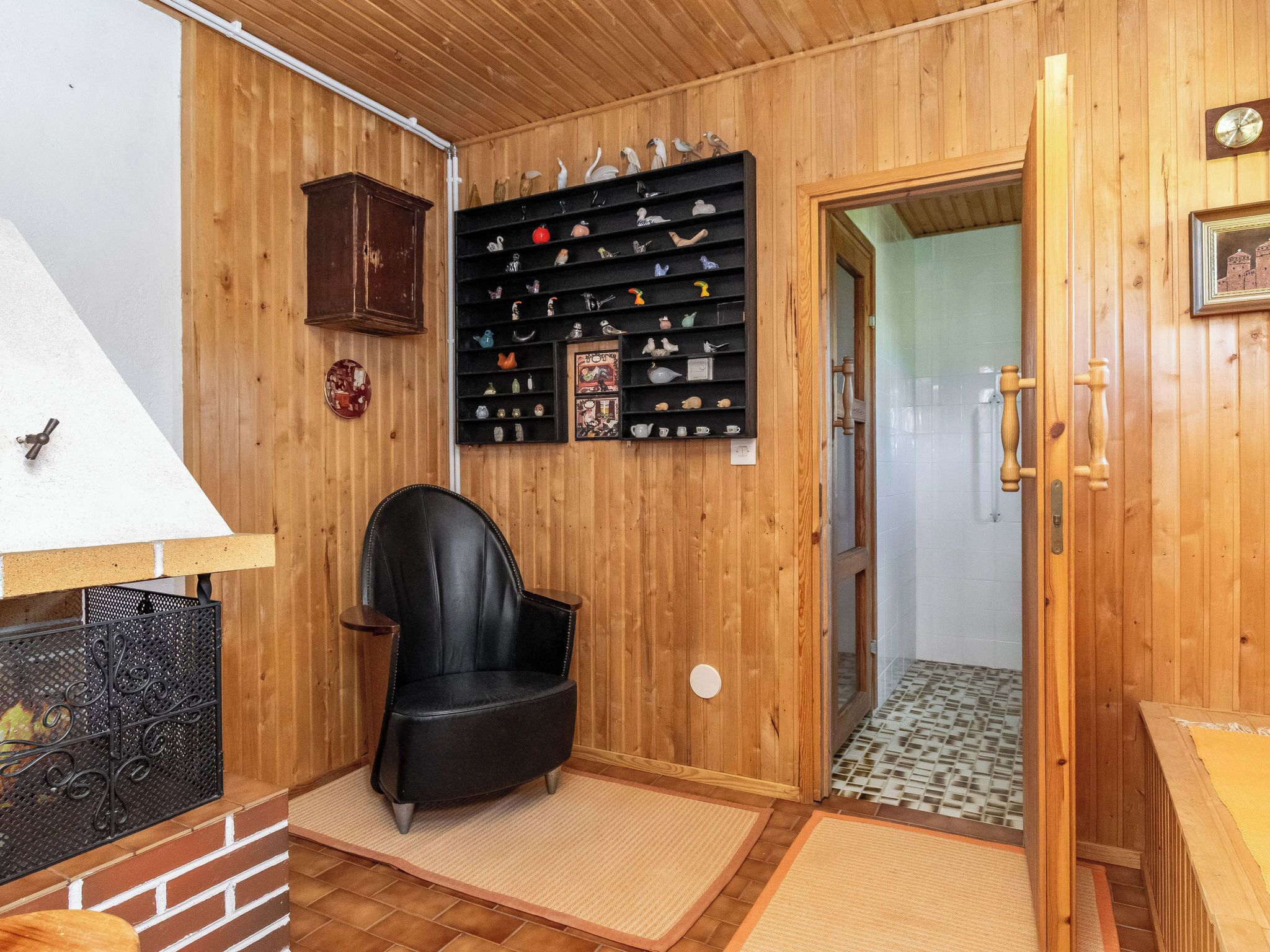 Un intérieur en bois, avec un fauteuil en cuir noir, une étagère ornée d’objets décoratifs et une porte donnant sur une autre pièce.