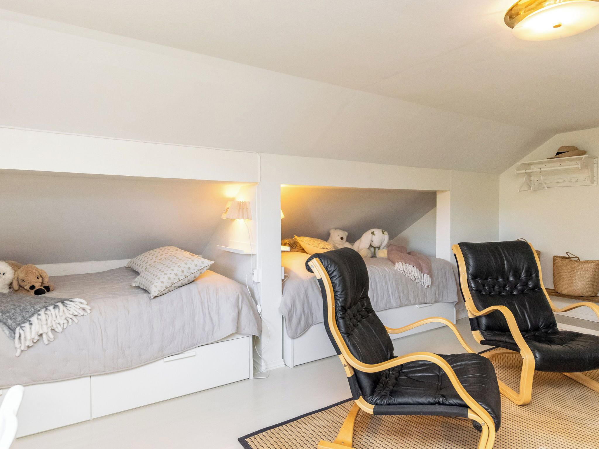 Ein Zimmer mit zwei Etagenbetten, einem schwarzen Ledersessel mit Holzgestell und einem weißen Regal mit einem Korb.