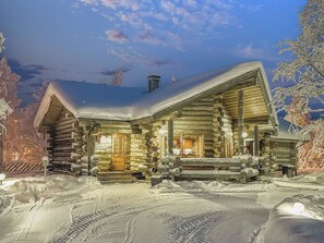 A log cabin with a snow-covered roof, a porch with a fire pit, and a visible chimney. - Talvihovi 5 by Interhome (Kuusamo)
