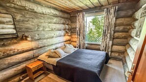 Ein Schlafzimmer in einer Blockhütte mit einem Bett, einem Nachttisch und einem Fenster mit Vorhängen.