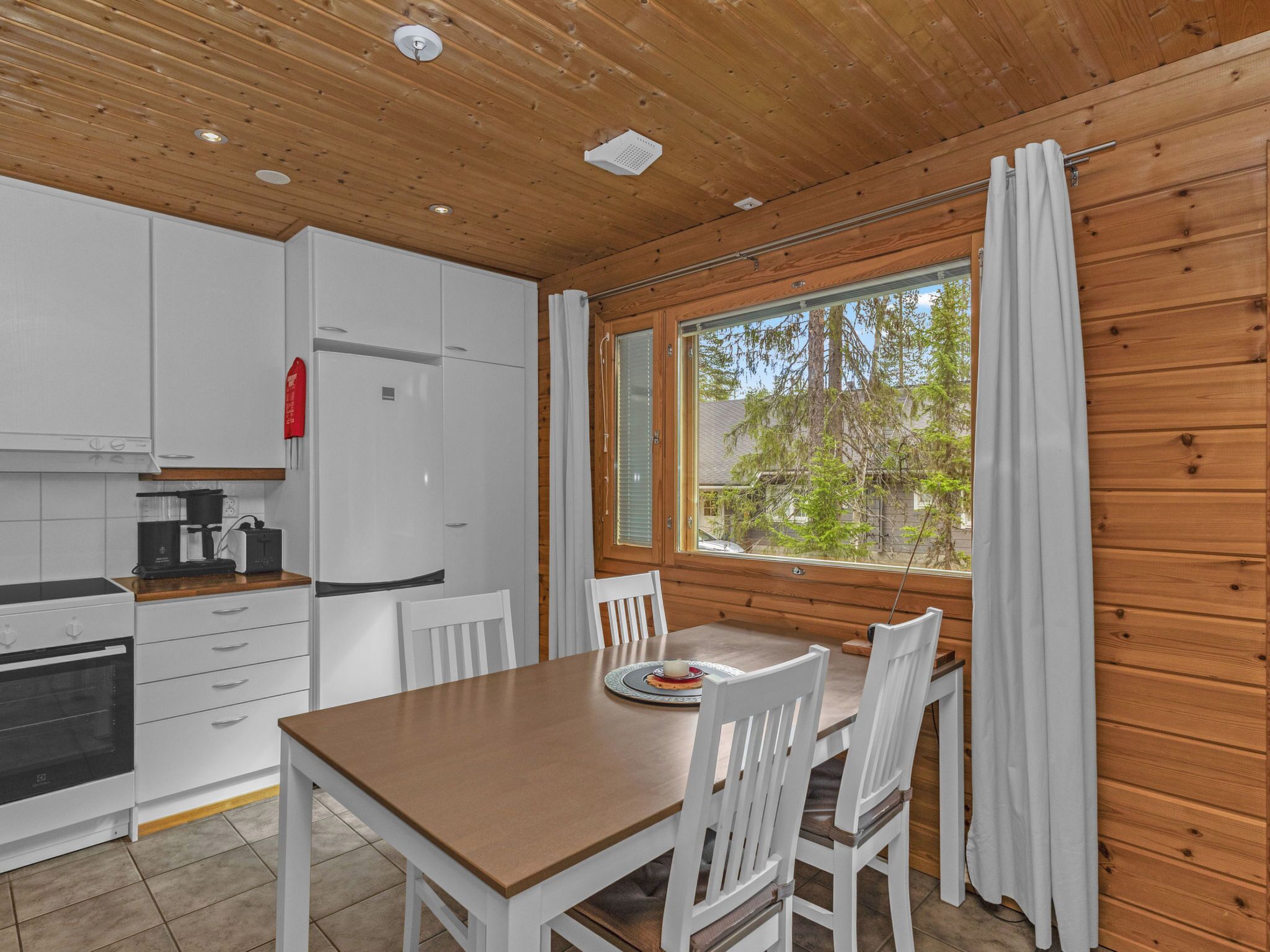 A modern kitchen with white cabinets, a built-in oven, and a dining area with a wooden table and white chairs.