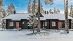 En toetages træhytte med mørk facade, en rød hoveddør og et snedækket landskab.