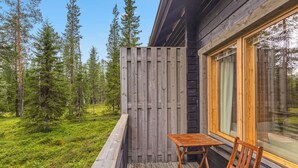 En træterrasse med et bord og en stol, omgivet af skov.