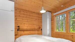 Et soveværelse med en seng, et hvidt skab, en hvid aircondition, et vindue med udsigt til træer og trævægge.