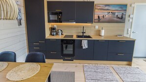 A modern kitchen with dark cabinets, a wooden countertop, and a painting of a sunset. - Niittyvilla by Interhome (Posio)