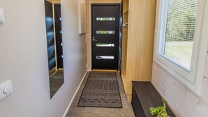 A hallway with a black door, a wooden bench, and a window with blinds. - Niittyvilla by Interhome (Posio)