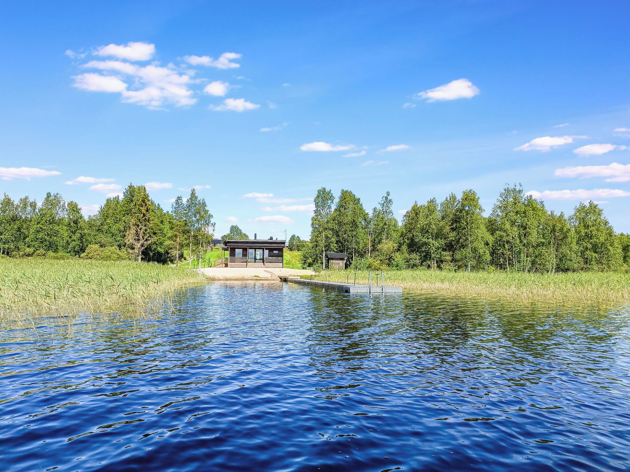 A lakeside property with a wooden dock, a covered seating area, and a forested backdrop.