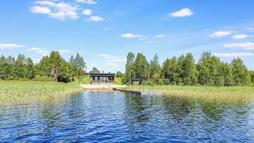 A lakeside property with a wooden dock, a covered seating area, and a forested backdrop.
