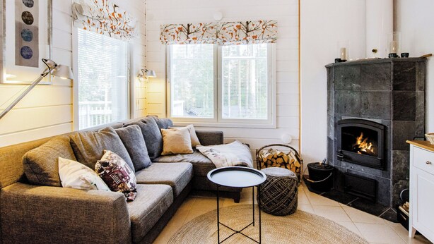 A cozy living room with a sectional sofa, a fireplace, and a small round table. - Saunaharju 6 by Interhome (Lieksa)