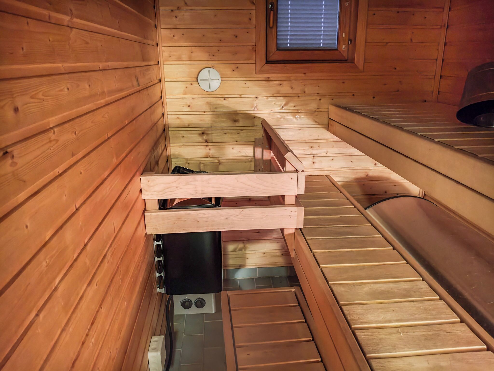 Un sauna en bois, avec des bancs, une petite fenêtre et un panneau de commande.