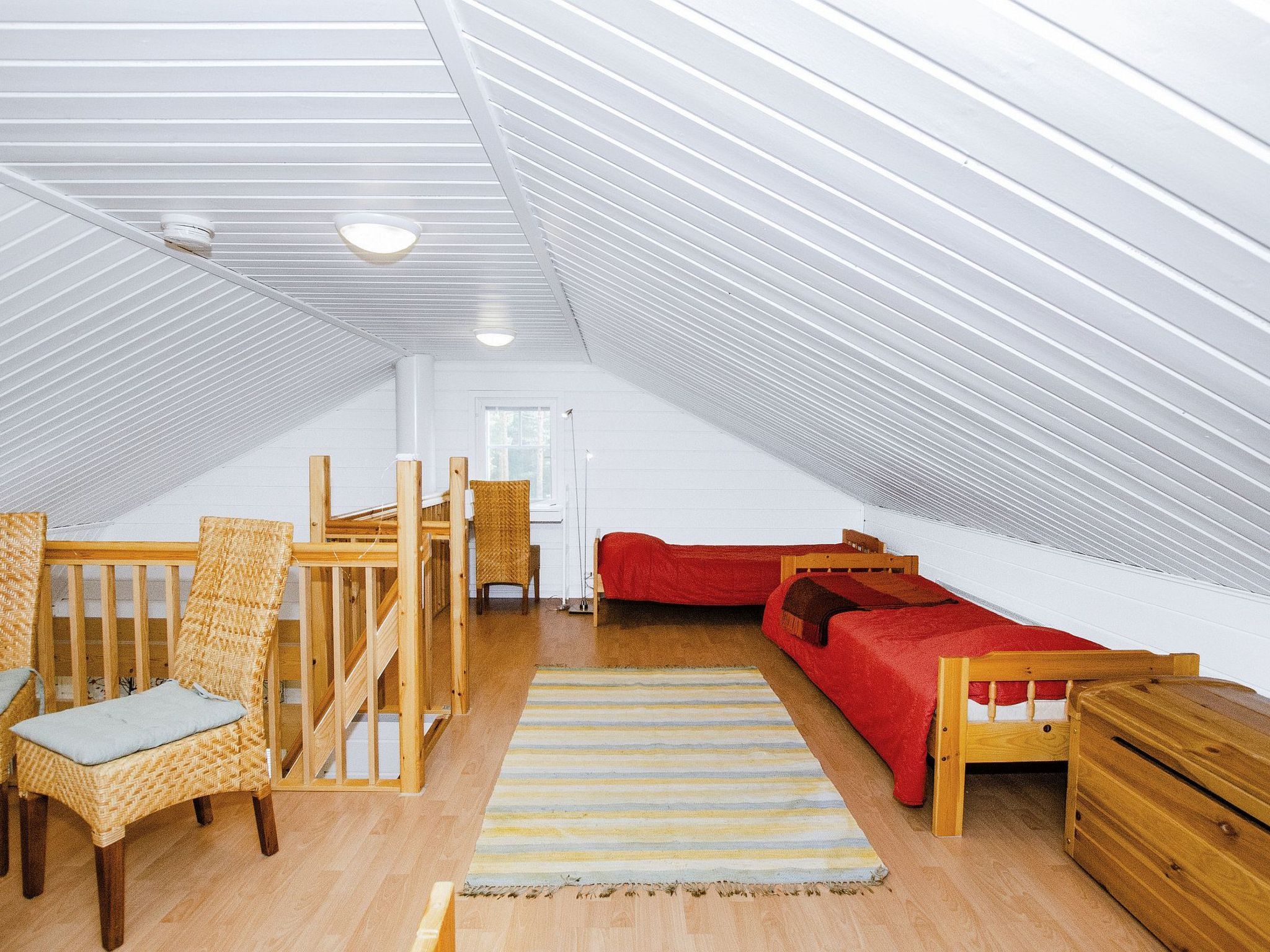 Ein geräumiges Dachzimmer mit hohen Decken, einem roten Sofa, einem Holzbett, einem Korbstuhl und einem kleinen Holztisch.