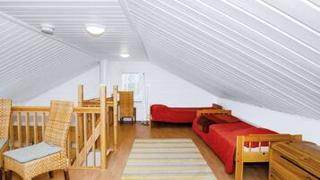 Ein geräumiges Dachzimmer mit hohen Decken, einem roten Sofa, einem Holzbett, einem Korbstuhl und einem kleinen Holztisch.