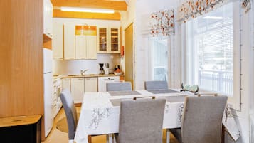 A modern kitchen with white cabinets, a dining table with grey chairs, and a window with blinds.