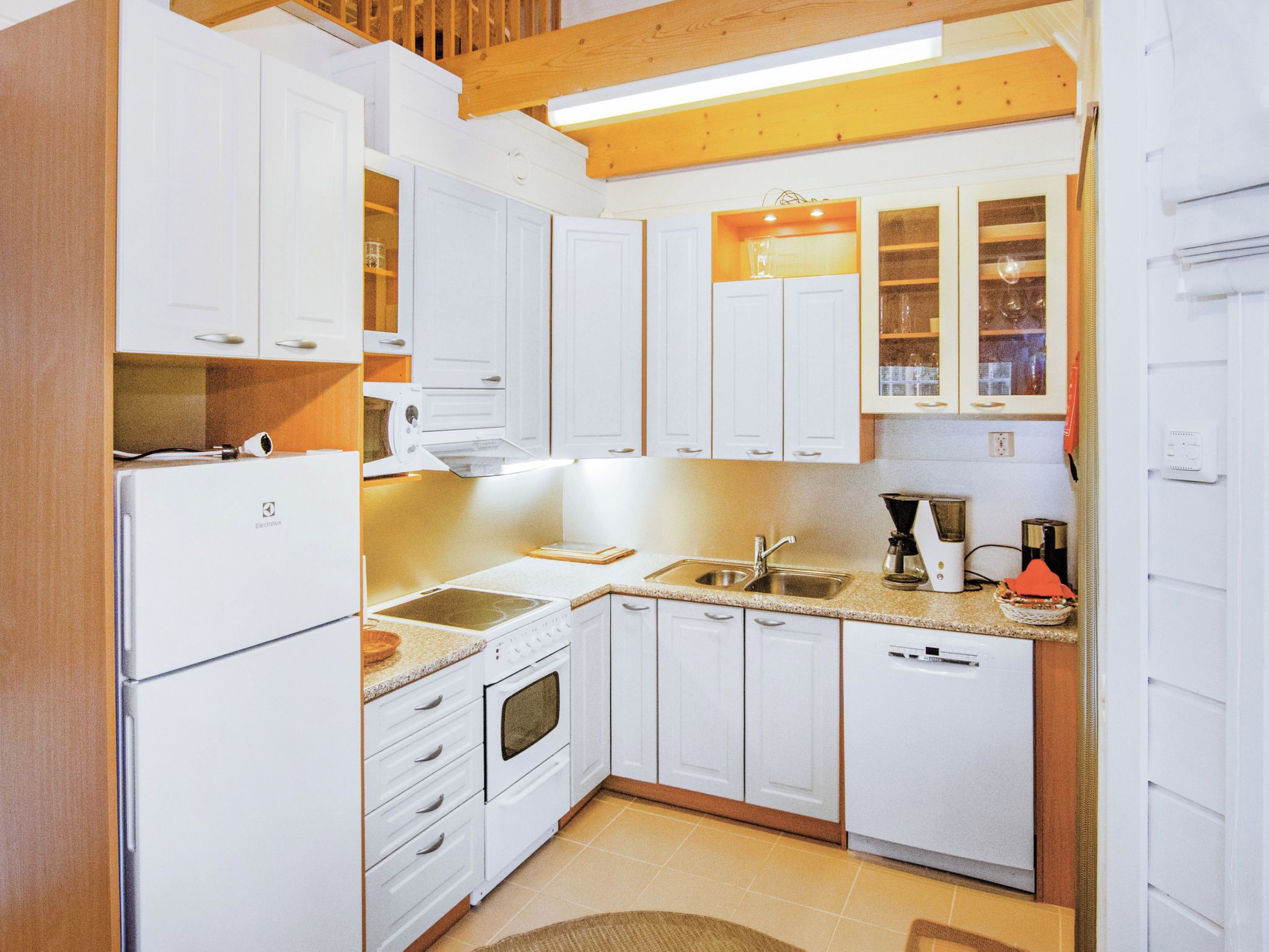 Una cocina compacta con gabinetes blancos, horno empotrado, cafetera y un lavabo.
