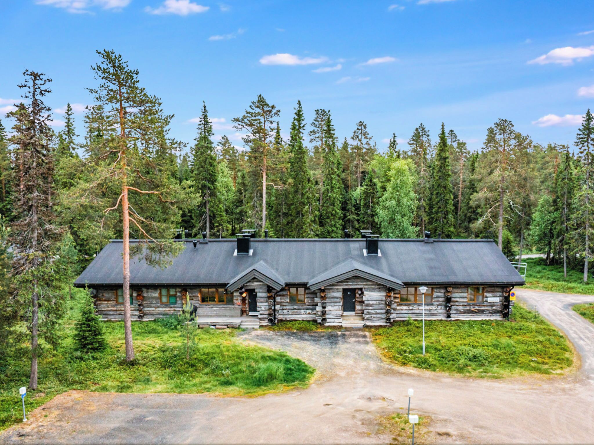 Une cabane en rondins avec une entrée principale au centre, deux entrées latérales et une véranda couverte.