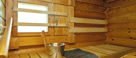 A wooden cabin interior with a bench, a metal bucket, and a window.