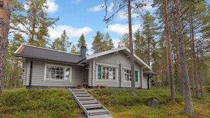 Une cabane en rondins avec un escalier en bois menant à l’entrée, entourée d’une forêt dense.