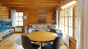 L’intérieur d’un chalet chaleureux, avec un plafond en bois, une table à manger ronde et un canapé.