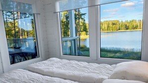 Une chambre à coucher avec un grand lit, deux fenêtres et une vue sur un lac et une forêt.