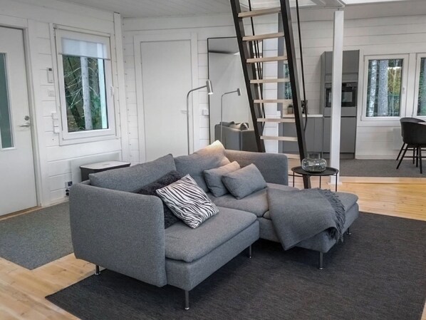 A modern living room with a grey sectional sofa, a small side table, a ladder, and a view of the kitchen through an open door. - Villa lokinkärki by Interhome (Orivesi)
