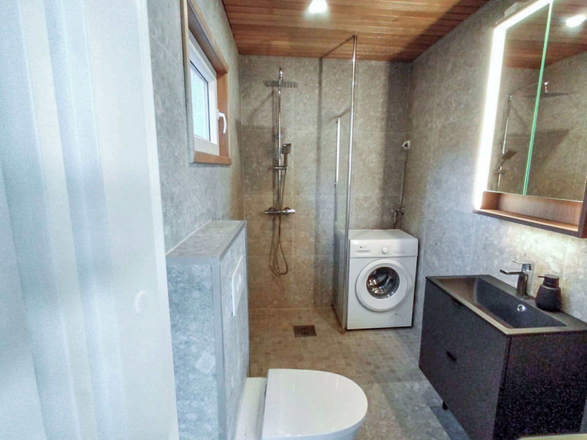 A compact bathroom with a shower, washing machine, and sink.