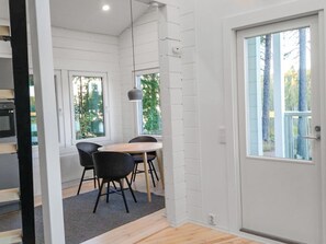 A modern interior with a dining area featuring a round table and black chairs, white walls, and large windows with a view of trees. - Villa lokinkärki by Interhome (Orivesi)