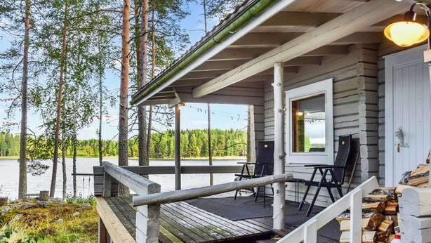 Une cabane en bois dotée d’une terrasse donnant sur un lac, entourée d’arbres.