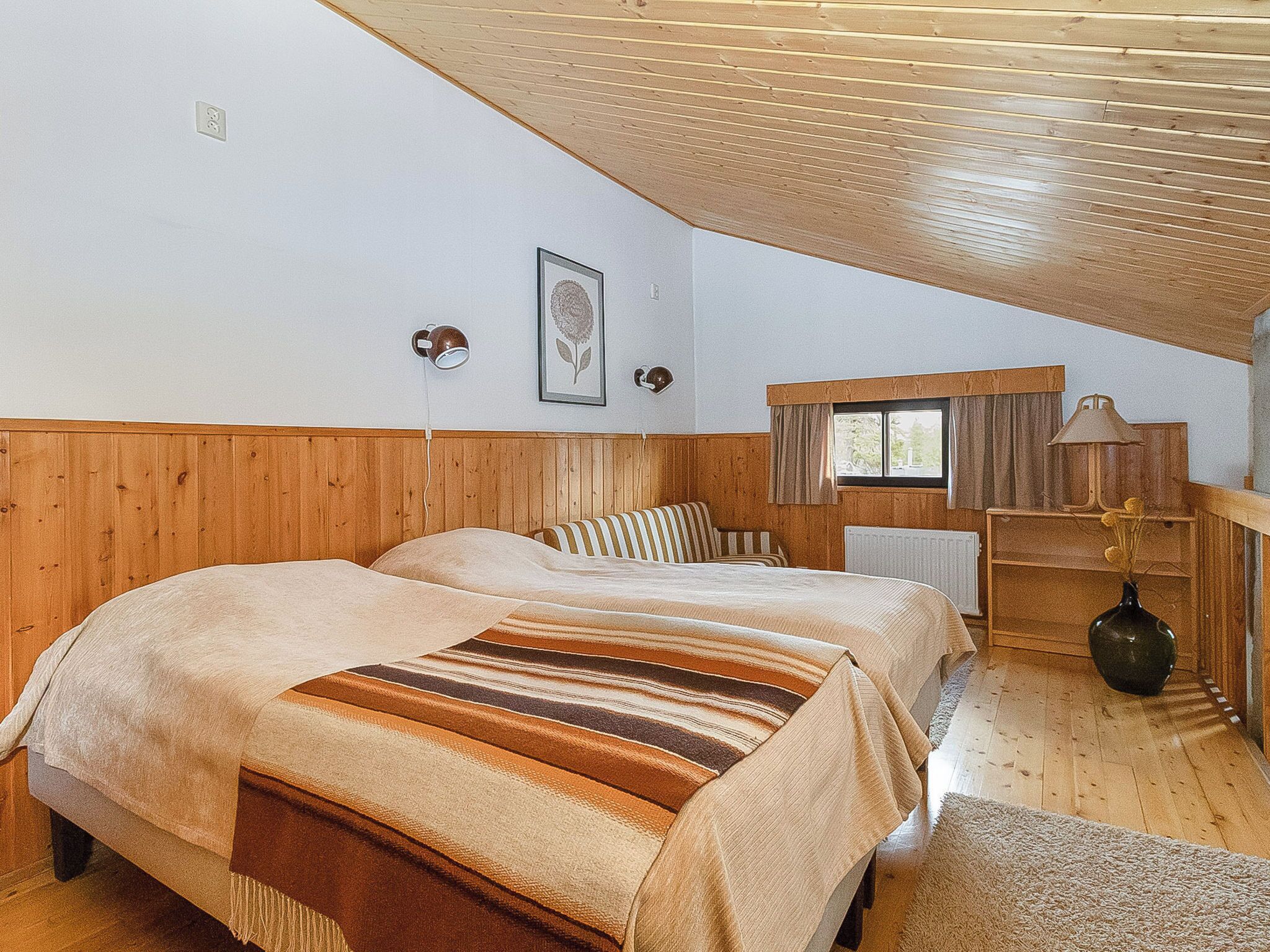 Una habitación con dos camas, paredes de madera, un ventanal, un radiador y una lámpara.