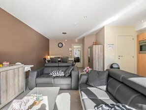 Ein modernes Wohnzimmer mit grauem Sofa, einem Esstisch und einer Küchenzeile im Hintergrund.