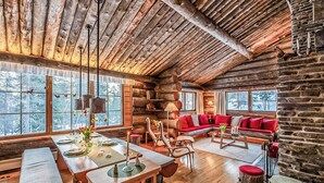 L’intérieur d’une cabane en rondins comprend un coin repas, un canapé et de grandes fenêtres donnant sur le paysage enneigé.