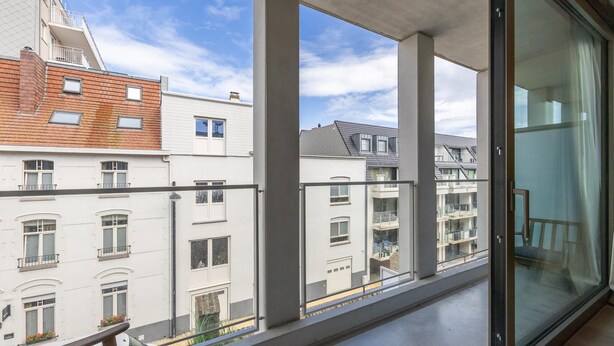 Un balcón con vistas despejadas a edificios cercanos, incluyendo una combinación de residencias y locales comerciales.
