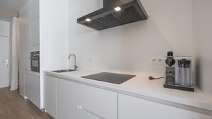 Una cocina moderna con gabinetes blancos, un lavamanos de acero inoxidable, un horno empotrado, una campana extractora y una cafetera.