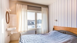 A bedroom with a bed, a window, a sink, and striped wallpaper. - Cosy flat near the centre (Koksijde)