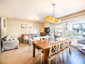 Un salon moderne avec une table à manger en bois, des chaises blanches, un canapé et un téléviseur.