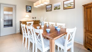 A dining area with a wooden table, white chairs, and a hanging light fixture. - Cosy flat near the centre (Koksijde)