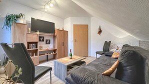 Ein modernes Wohnzimmer mit einer Couch, einem Fernseher, Holzschränken und einer Deckenleuchte.