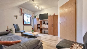 Ein gemütliches Wohnzimmer mit einer Couch, einem Sessel, einem Couchtisch, einem Fernseher und einem Kleiderschrank.