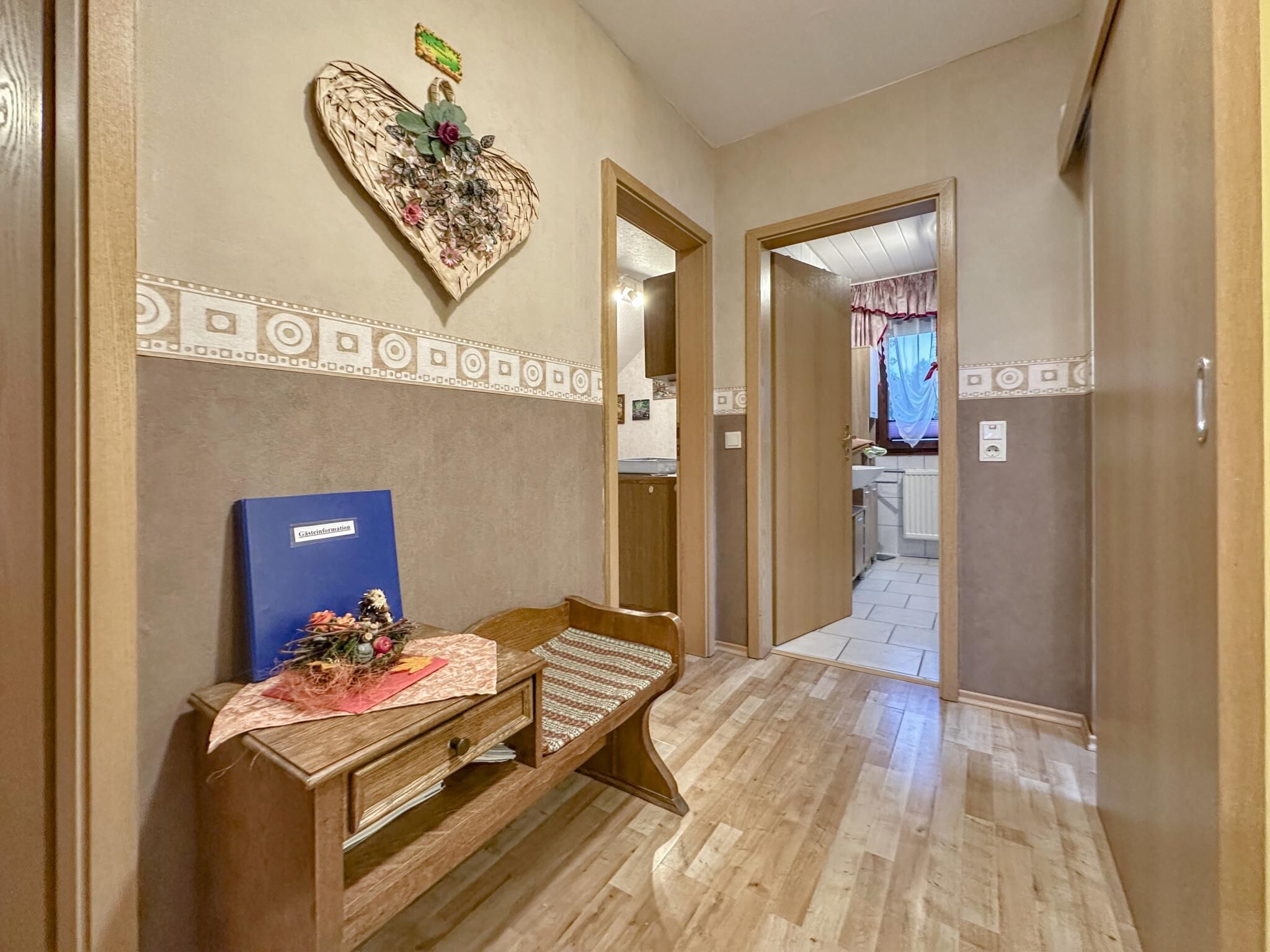 A hallway with a wooden bench, a decorative heart-shaped wall piece, and a blue information board.
