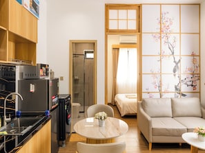 A compact hotel room with a kitchenette, a dining area, a sofa, and a traditional Japanese-style sliding door. - GO VILLA by DNM Hospitality (Ho Chi Minh)