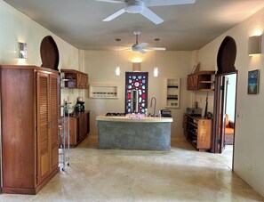 A kitchen with a central island, wooden cabinets, a ceiling fan, and a stained glass door. - Casa Maroc Jungle Escape with Yoga Shala in Montezuma |Tropical Garden. (Montezuma)