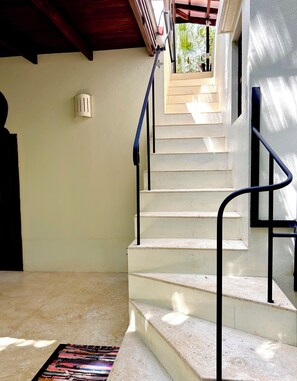 A staircase with a handrail leading to an upper level, a light fixture on the wall, and a patterned rug on the floor. - Casa Maroc Jungle Escape with Yoga Shala in Montezuma |Tropical Garden. (Montezuma)