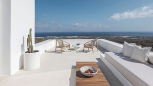 A rooftop terrace with white walls, two wicker chairs, a small table, a bowl of fruit, and a view of the ocean. - Charisma Estate Villa (Oia)