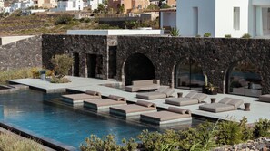 Zona junto a la piscina con varias sillas de descanso y una pared de piedra.