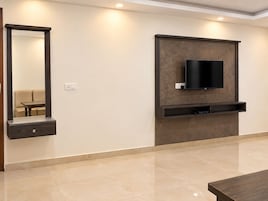 Una sala de estar moderna con un televisor de pantalla plana montado en la pared, un banco empotrado debajo y un espejo grande a la izquierda.
