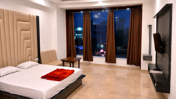 A hotel room with a bed, a small table, a chair, a TV, and a view of the city at night.