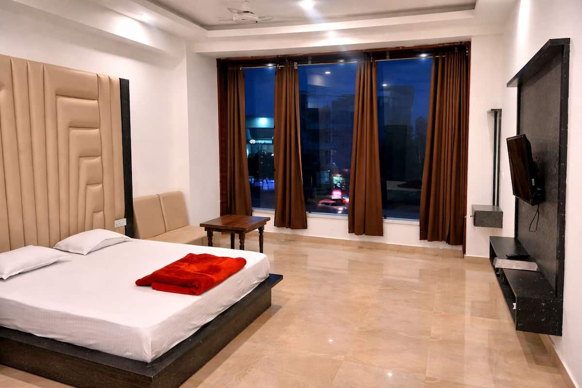 A hotel room with a bed, a small table, a chair, a TV, and a view of the city at night.